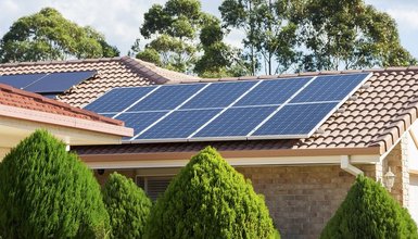 Haus mit Büschen und Solarzellen auf dem Dach in der Sonne