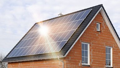 Rotes Backsteinhaus schräg seitlich mit Solarmodulen auf dem Dach, auf die die Sonne scheint