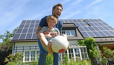 Vater mit Kind und Ball am spielen im Garten eines Hauses mit Solarzellen auf dem Dach