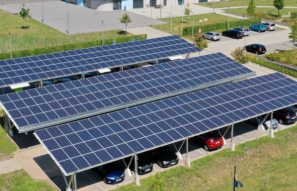 Solar-Carports mit Photovoltaikanlagen auf Parkplätzen vor einem Bürogebäude; im Hintergrund Wohnhäuser mit Solardächern.