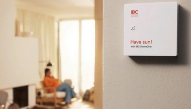 Aufnahme eines Wohnzimmers unscharf im Hintergrund; Vordergrund zeigt beige Wand mit angebrachtem Energiemanagement System mit Schrift "Have sun!"