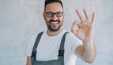 Erfreuter Mann mit Brille in Latzhose der das Taucherzeichen für "OK" zeigt