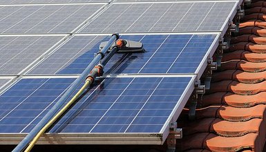 Nahaufnahme eines Dachs mit roten Ziegeln und Solarmodulen, auf den Modlen ein Reinigungsgerät