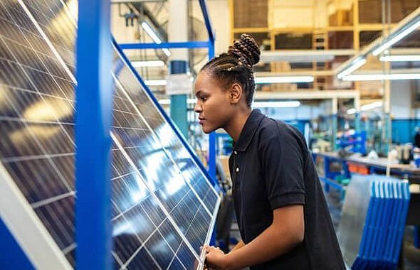 Person schiebt PV Modul durch Lagerhalle, im Hintergrund noch mehr Module