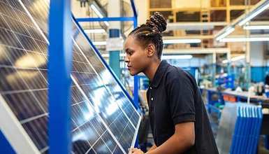 Person schiebt PV Modul durch Lagerhalle, im Hintergrund noch mehr Module